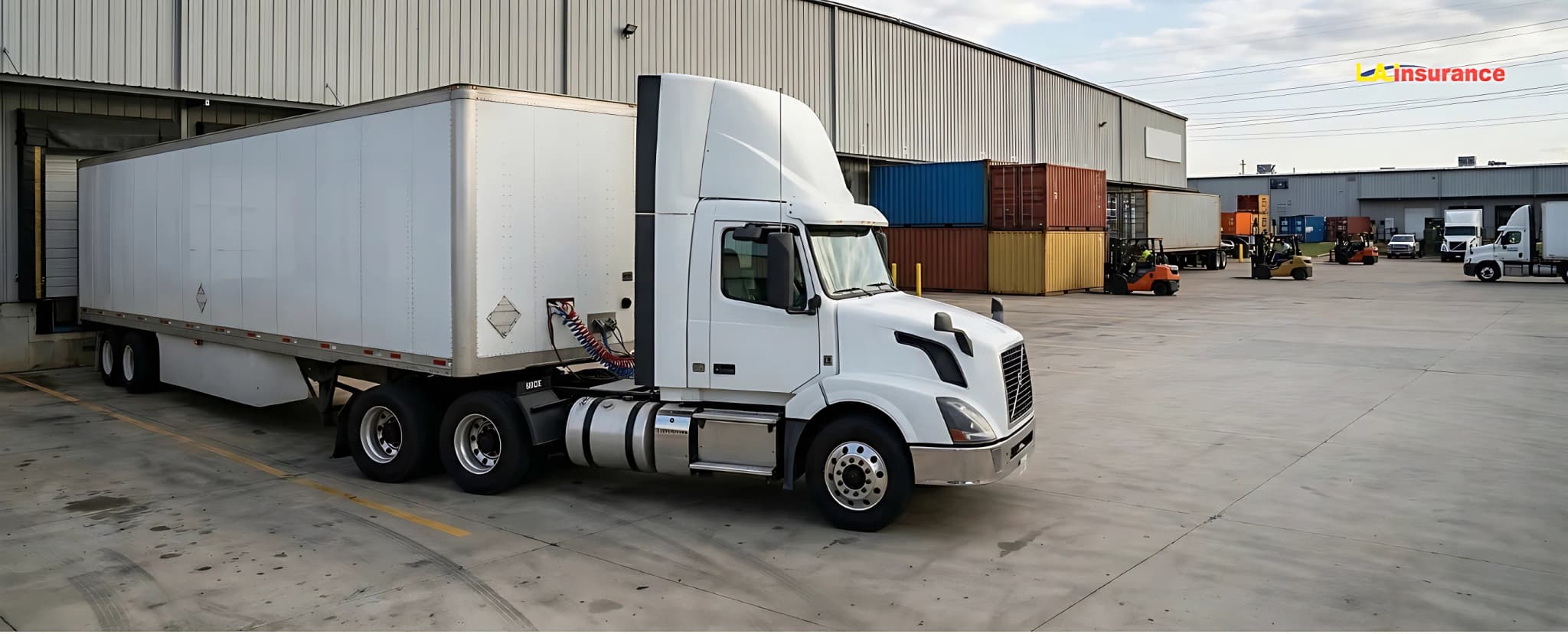 Are Trailers Covered Under Commercial Auto Insurance? White semi-truck with attached cargo trailer parked at a commercial warehouse loading dock, representing commercial auto insurance coverage for trailers.